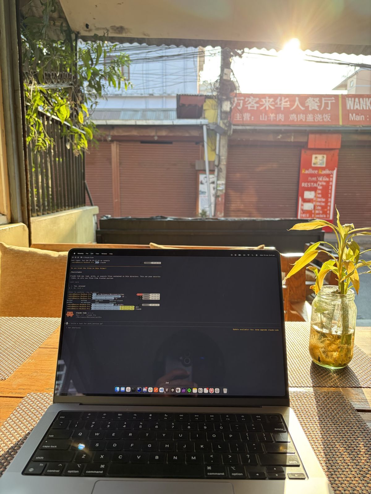 A laptop on a sunlit café terrace, terminal open, with shopfronts across the street